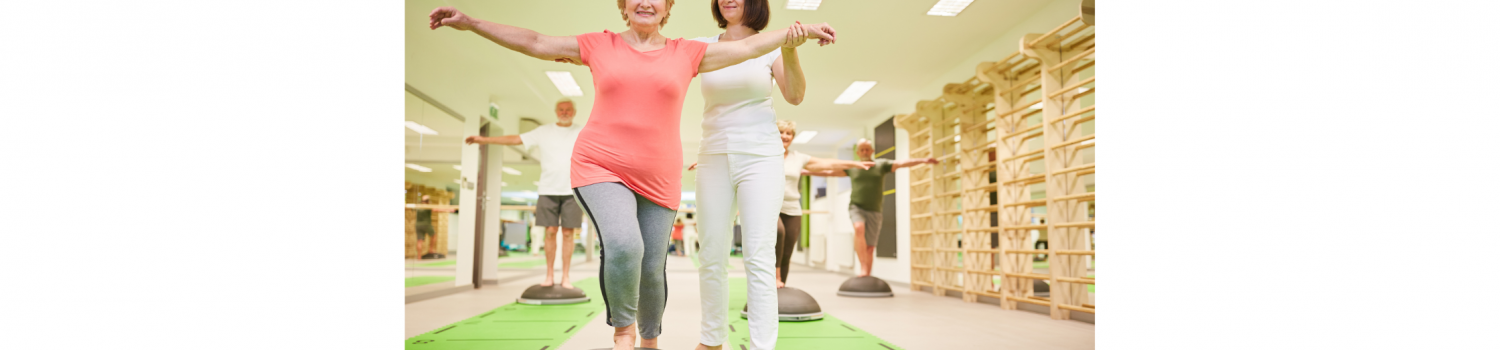 Trainer helps senior woman with balance training on the Bosu Ball in a fitness class