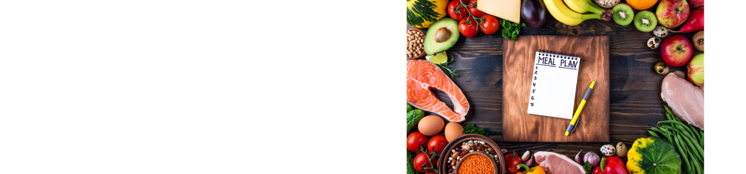 A wooden table layout with healthy foods such as fresh fruits and vegetables, different kinds of meat, nuts, and grains along the edges, and a notebook with a “meal plan” list written on it next to a pen in the center on top of a wooden cutting board